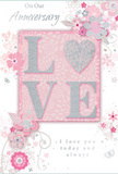 The anniversary card shown here exudes a sense of cherished intimacy, as if it belongs beside a vase of fresh flowers in an Old Ford kitchen after a special delivery. At its centre, the word LOVE is presented in raised, glittered letters, with the soft sparkle of blush pink and silver giving each letter a gentle halo. The shapes are smooth and inviting, and the textured finish suggests a pleasing, almost velvety feel under the fingertips. Surrounding this central word, a trail of delicate blooms and curling tendrils unfurls across the card's surface. The flowers are small, with rounded petals and fine stems, drawn in slender lines and shaded in watercolor-soft tones of pastel pink, mauve, ivory, and pale grey. These shades recall the muted elegance of anniversary bouquets ordered for delivery around Old Ford, Bow, and the nearby canals. The background is a smooth, pale pink wash that quiets the eye and makes the floral details and shimmering letters stand out without strain. Scattered among the blossoms are tiny flourishes-loose petals, swirling lines, and discreet butterfly silhouettes-that add movement and a touch of whimsy, like petals stirring in a light breeze in Victoria Park. The words On Our Anniversary and a loving line such as I love you today and always are inscribed in fine, understated script, spaced generously so each phrase feels thoughtful and sincere. Altogether, the card gives the impression of a softly spoken promise, tender and enduring, the paper counterpart to a pastel-toned bouquet chosen to celebrate years of shared laughter and quiet companionship in this corner of East London.
